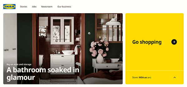 IKEA homepage showcasing a bathroom with dark walls, a white vanity, and pink flowers. A headline reads "A bathroom soaked in glamour." Dive into furniture shopping with the best furniture selections on the yellow section: "Go shopping.